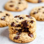 A stack of delicious almond flour chocolate chip cookies with a bite taken out of the top one, revealing gooey chocolate and sprinkled with sea salt.