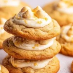 A close-up shot of a stack of three golden banana pudding cookies, topped with creamy frosting and delightful candy pieces.