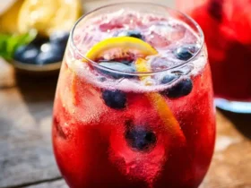 A glass of refreshing blueberry lemonade garnished with lemon slices and fresh blueberries on a rustic wooden table.