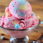 A vibrant bowl of bubblegum ice cream featuring pink, blue, and yellow swirled scoops, adorned with colorful candies on a wooden table.