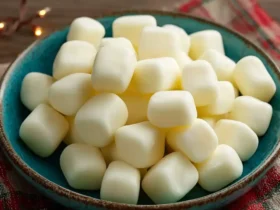A teal bowl overflowing with creamy white butter mints, resting on a plaid napkin with festive lights in the background.