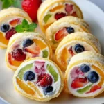Close-up of vibrant Cheesecake Fruit Roll-Ups filled with fresh berries, kiwi, and mango slices, beautifully arranged on a white plate.