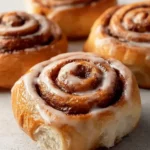 Close-up of several warm, glazed Coffee Cinnamon Rolls, with one in the foreground showing a soft, delicious interior.