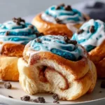 Soft Cookie Monster Cinnamon Rolls with vibrant blue & white icing, chocolate crumbles, on a plate, one with a bite revealing its swirl.