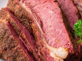 Close-up of perfectly sliced Corned Beef Brisket with a flavorful crust and a sprig of parsley on a white plate.