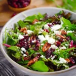 A vibrant Cranberry & Goat Cheese Salad in a white bowl, featuring fresh mixed greens, pecans, and dried cranberries.