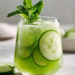 A refreshing glass of Cucumber Mint Agua Fresca with cucumber slices, mint sprig, and bubbly green liquid on a light background.