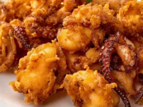 A close-up shot of a plate piled high with golden-brown Fried Baby Octopus, garnished with a lemon wedge.