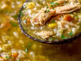 A ladle lifts a spoonful of hearty Green Chile Chicken Stew, filled with shredded chicken, rice, corn, and carrots.