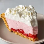A tempting slice of Homemade Strawberry Cream Pie with a golden graham cracker crust, fresh strawberry layer, pink cream filling, and whipped cream topping.
