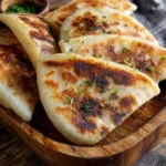 A close-up view of several golden-brown Irish Potato Farls, garnished with fresh chives, served on a rustic wooden board.