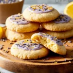 A stack of iced Lemon Lavender Cookies on a wooden board, with one cookie broken open to reveal its soft texture.
