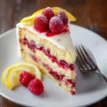 A tempting slice of lemon raspberry cake on a white plate, garnished with fresh raspberries and lemon slices.