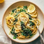 A close-up of a bowl of Lemon Swiss Chard Pasta, garnished with grated cheese and a fresh lemon slice, with a fork.
