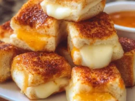 A close-up view of golden-brown Mini Grilled Cheese Hawaiian Rolls piled on a white plate, with gooey melted cheese oozing from the sides.