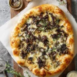 A delicious golden-crusted morel mushroom pizza topped with melted cheese, fresh thyme, and roasted garlic on a wooden board.