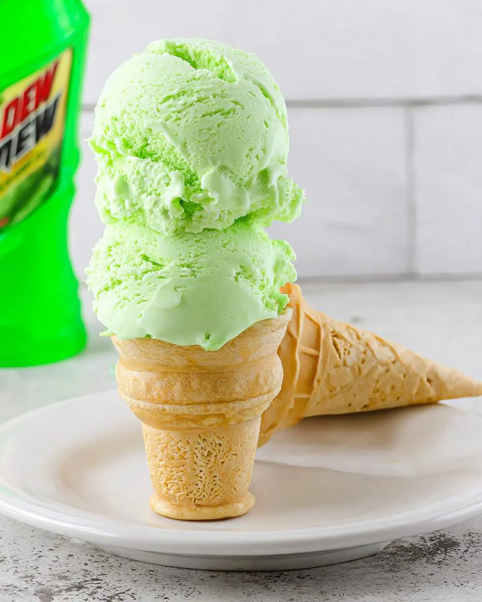 Two scoops of vibrant green Mountain Dew ice cream in a waffle cone, with a Dew bottle visible in the background.