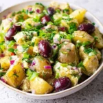 A vibrant bowl of Olive Greek Potato Salad, featuring tender new potatoes, dark olives, red onion, and fresh dill, dressed in a creamy sauce.