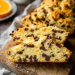Sliced Orange Chocolate Chip Scone Bread on a wooden board, showcasing its moist crumb filled with chocolate chips.