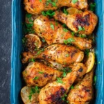 A vibrant overhead shot of delicious Oven Roasted Chicken Drumsticks, garnished with fresh parsley and lemon slices in a blue baking dish.