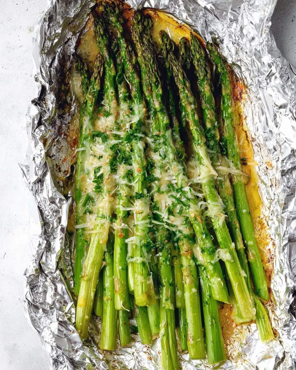 Parmesan grilled asparagus 28 A close-up of delicious Parmesan grilled asparagus topped with melted cheese and fresh herbs, served in aluminum foil.