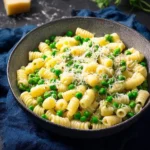 A close-up of a delicious Pasta and Peas Recipe in a grey bowl, topped with grated Parmesan cheese and fresh herbs on a dark surface.