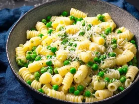 A close-up of a delicious Pasta and Peas Recipe in a grey bowl, topped with grated Parmesan cheese and fresh herbs on a dark surface.