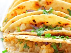 A close-up view of golden-brown potato tacos filled with seasoned potatoes, red onions, and fresh cilantro, served on a white plate.