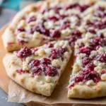 A delicious Raspberry Cheesecake Dessert Pizza with a slice cut out, showcasing a creamy base, fresh raspberries, and crumble topping.
