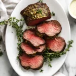 Perfectly cooked Roast Beef Tenderloin, sliced to reveal a medium-rare center, garnished with fresh thyme on a white platter.