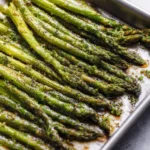 A close-up shot of perfectly seasoned and tender roasted asparagus spears glistening on a metal baking sheet.