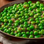 A close-up shot of a rustic bowl filled with bright green sauteed green peas mixed with tender caramelized onions.