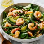 A close-up shot of a vibrant Shrimp Asparagus Salad in a white bowl, featuring cooked shrimp, green asparagus, and avocado slices.
