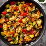 A close-up view of a pan filled with vibrant Skillet Chicken With Vegetables, garnished with fresh herbs, ready to serve.