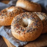 A close-up shot of freshly baked sourdough discard bagels, heavily topped with everything seasoning, on a wooden board.