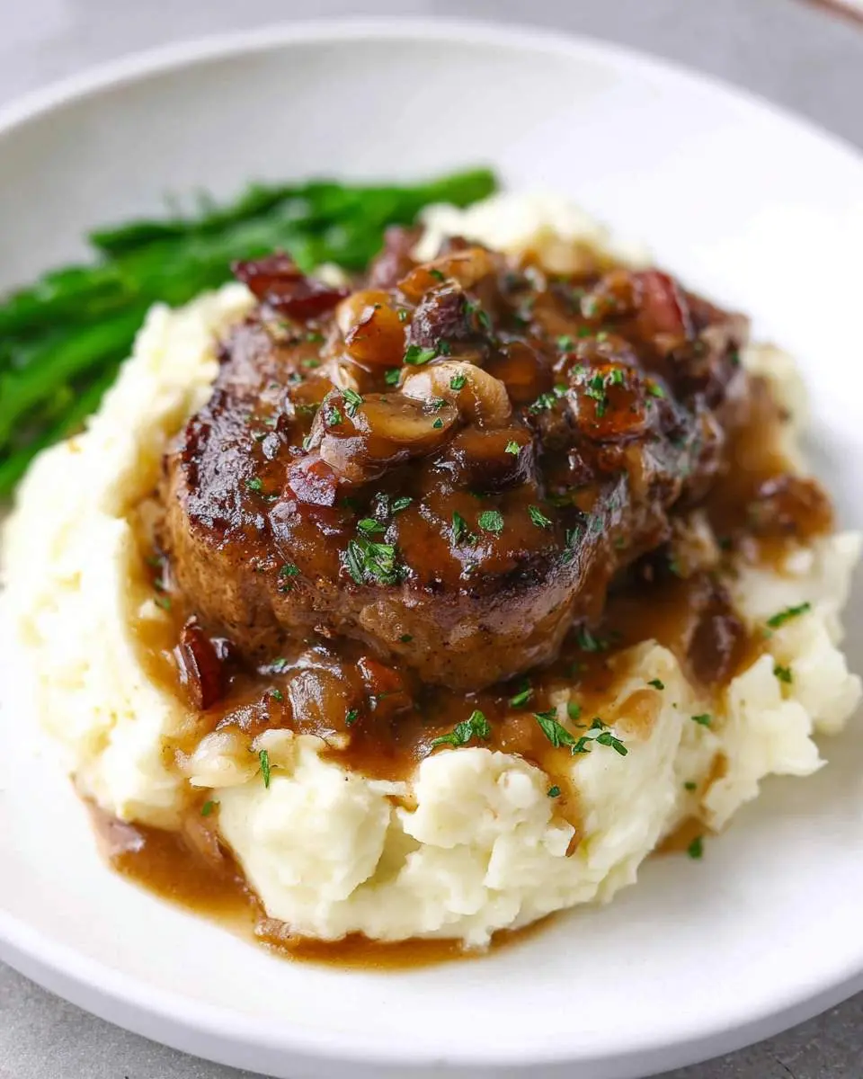 A close-up of a delicious steak and mashed potatoes dish, topped with savory mushroom and bacon gravy, served with green beans.