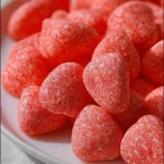 A close-up shot of a pile of bright red strawberry foam candies on a white plate, showcasing their soft, textured surface.