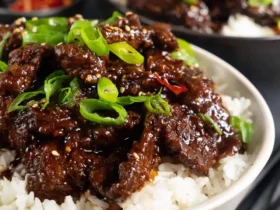 teriyaki beef 55 A bowl of teriyaki beef served over white rice, garnished with sliced green onions and sesame seeds.