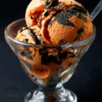 Scoops of vibrant orange and black swirled Tiger Tail Ice Cream served in a clear glass sundae dish.