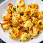 Golden crispy Air Fryer Tortellini served on a white plate, garnished with fresh herbs and grated cheese.