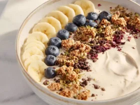 Creamy banana smoothie bowl topped with sliced bananas, blueberries, granola, and chocolate chunks in a ceramic bowl.