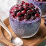 Berry Chia Pudding topped with fresh blueberries and raspberries in a glass cup with a spoon beside it.