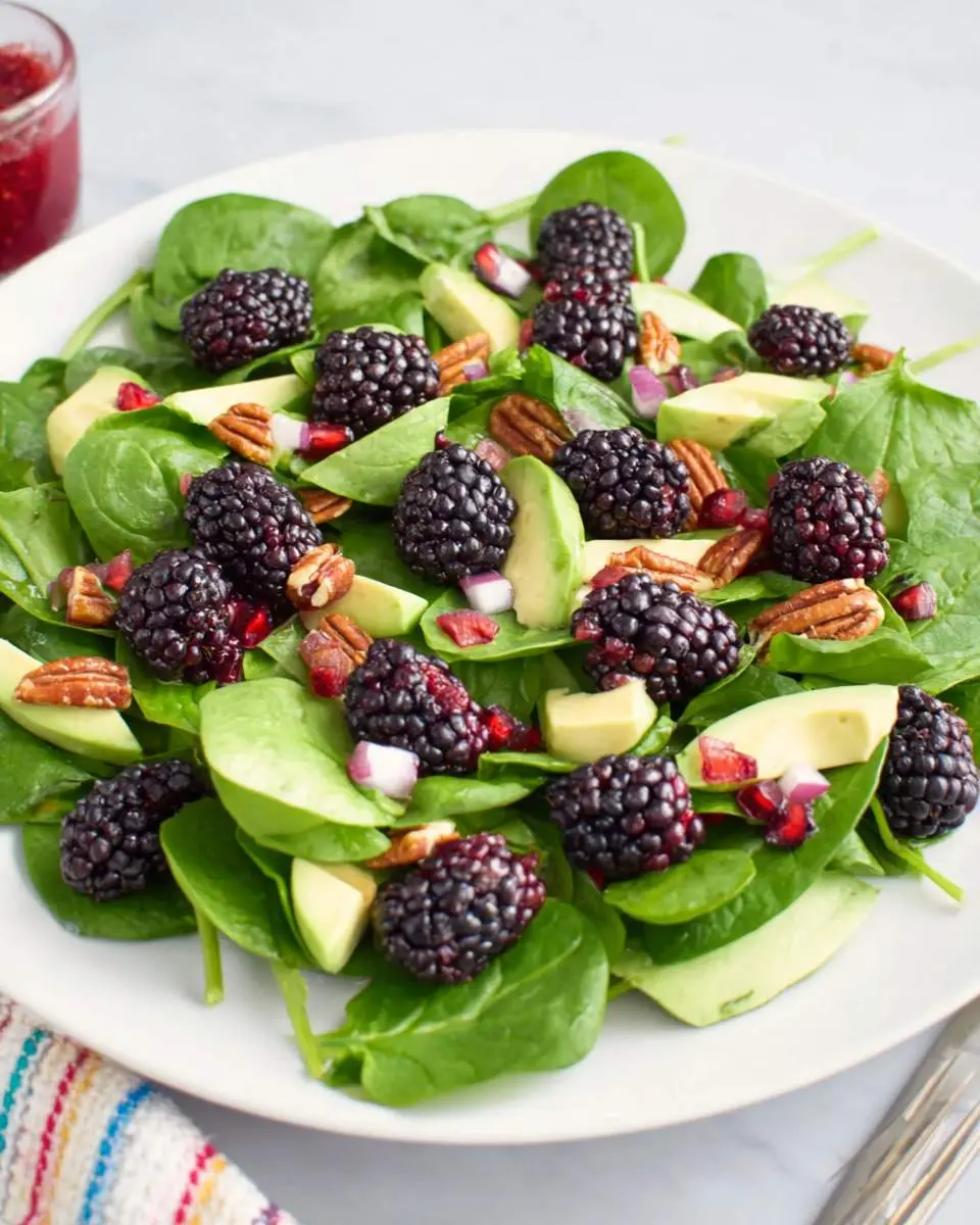 Fresh Blackberry Spinach Salad with avocado, pecans, and red onion on a white plate.