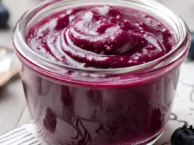 Blueberry curd 52 A glass jar filled with smooth, vibrant purple blueberry curd, surrounded by fresh blueberries.