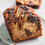Sliced Chocolate Caramel Banana Bread with gooey caramel drizzle and banana slices on top, served on a white plate.