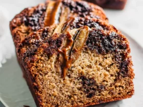 Sliced Chocolate Caramel Banana Bread with gooey caramel drizzle and banana slices on top, served on a white plate.