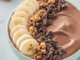 Chocolate Peanut Butter Smoothies Recipes Bowl topped with banana slices, granola, and chocolate chips in a blue bowl.