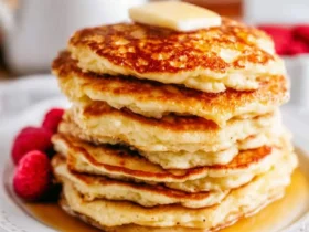 Stack of golden cottage cheese pancakes topped with butter and maple syrup, served with fresh raspberries.