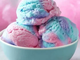 Three scoops of colorful Cotton Candy Ice Cream in a blue bowl with pink and blue swirls.