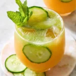 A refreshing glass of Cucumber Melon Agua Fresca garnished with mint, cucumber slices, and ice on a marble surface.